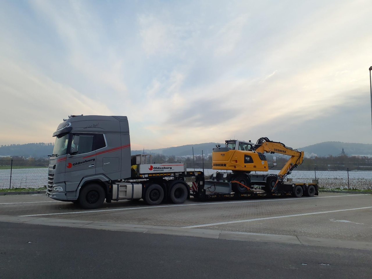 Grauer Lastwagen transportiert gelben Bagger auf einem Tieflader.